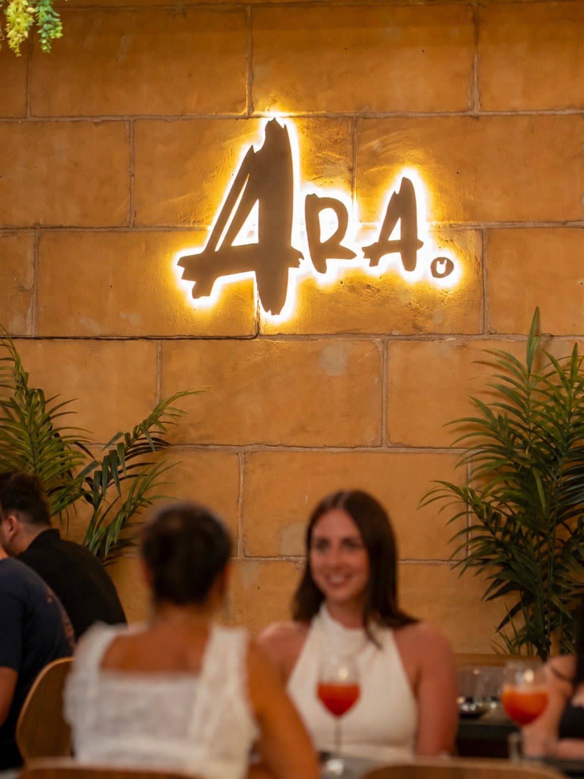 Dos clientas brindando junto al rótulo iluminado de ARA.