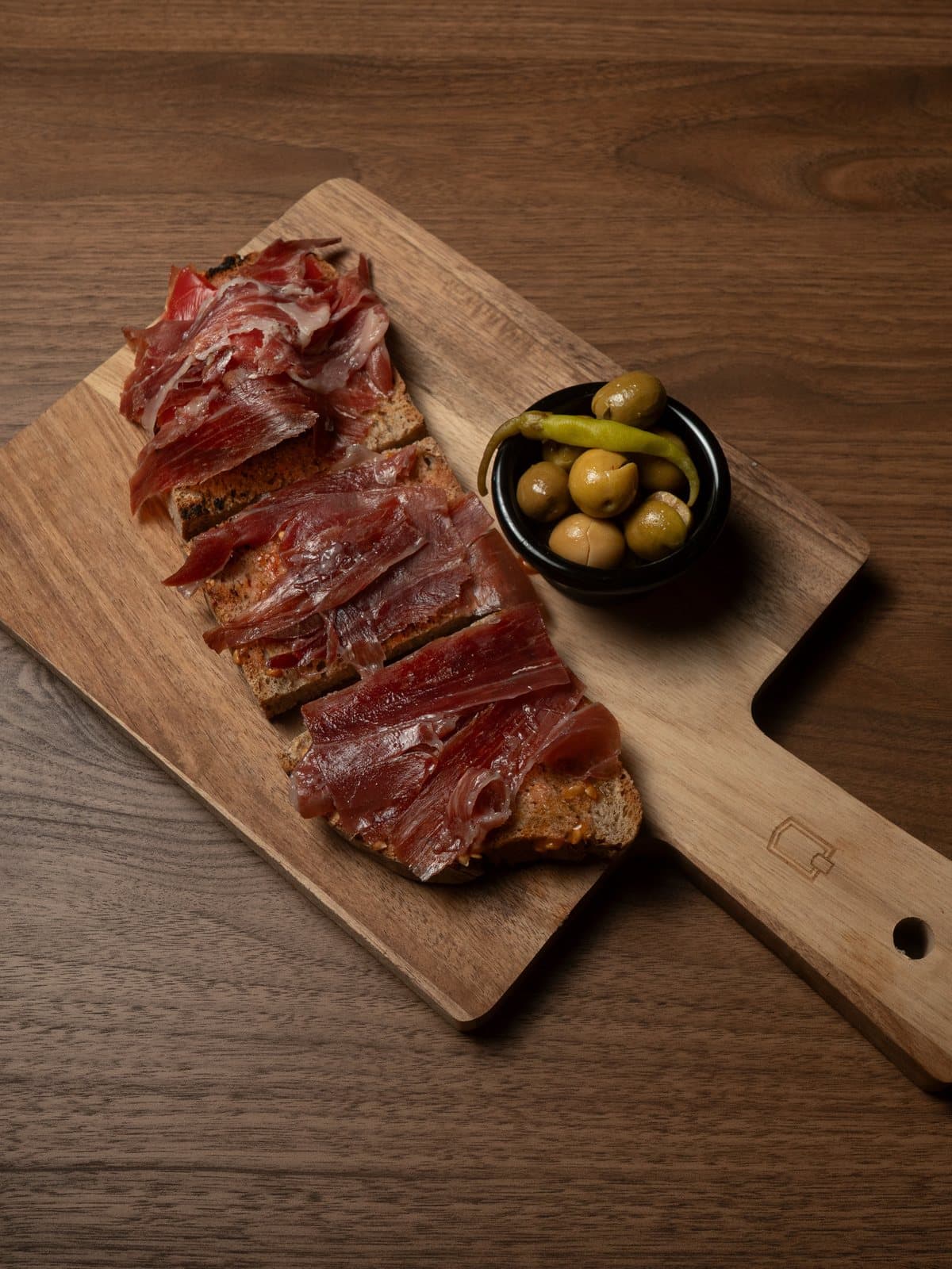 Ración de jamón ibérico sobre tabla de madera con olivas